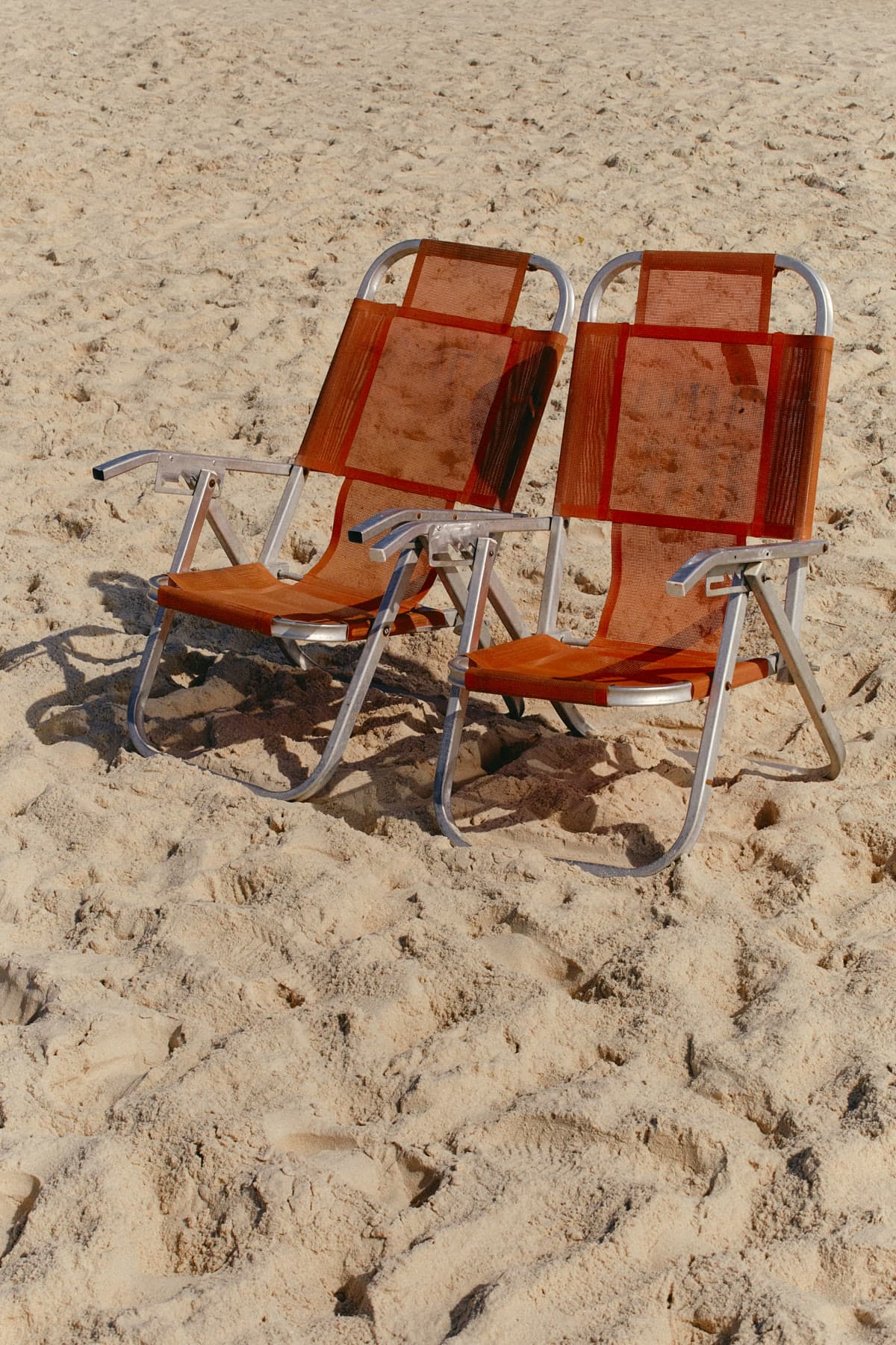 Two orange beach chairs on sand, photographed with open space around them.